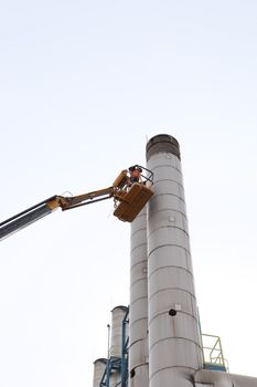 A worker performs maintenance on tall smokestack in İzmir's industrial district.