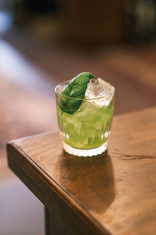 Free A close-up of a vibrant green cocktail with ice and a leaf garnish on a wooden table. Stock Photo