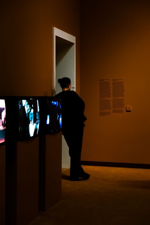 Free A person stands in a dimly lit museum, engaging with a modern art exhibit. Stock Photo