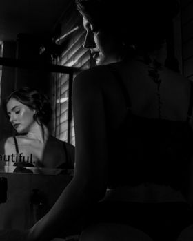 A woman reflects in a mirror in a moody black and white portrait, showcasing emotion and introspection.