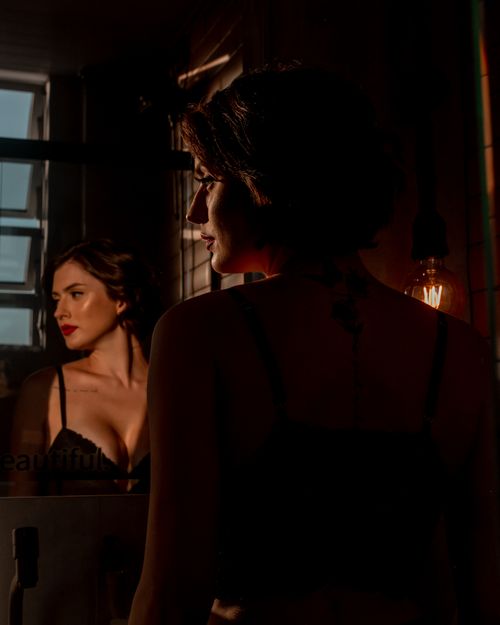 Free A stylish woman in lingerie gazes at her reflection in a dimly lit room, creating a dramatic and contemplative mood. Stock Photo
