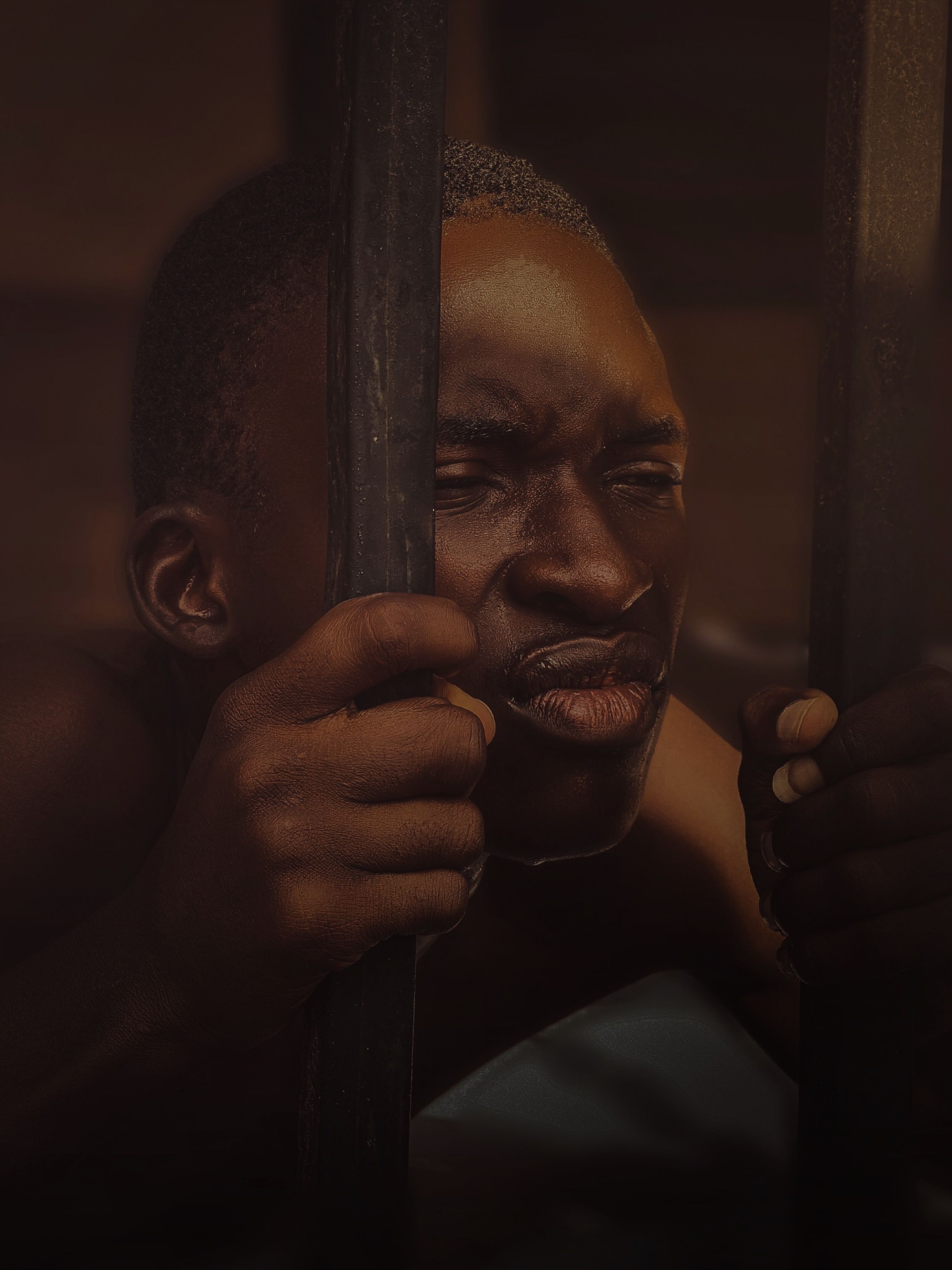 A thought-provoking portrait of a man holding bars, captured with deep emotion and shadow play.
