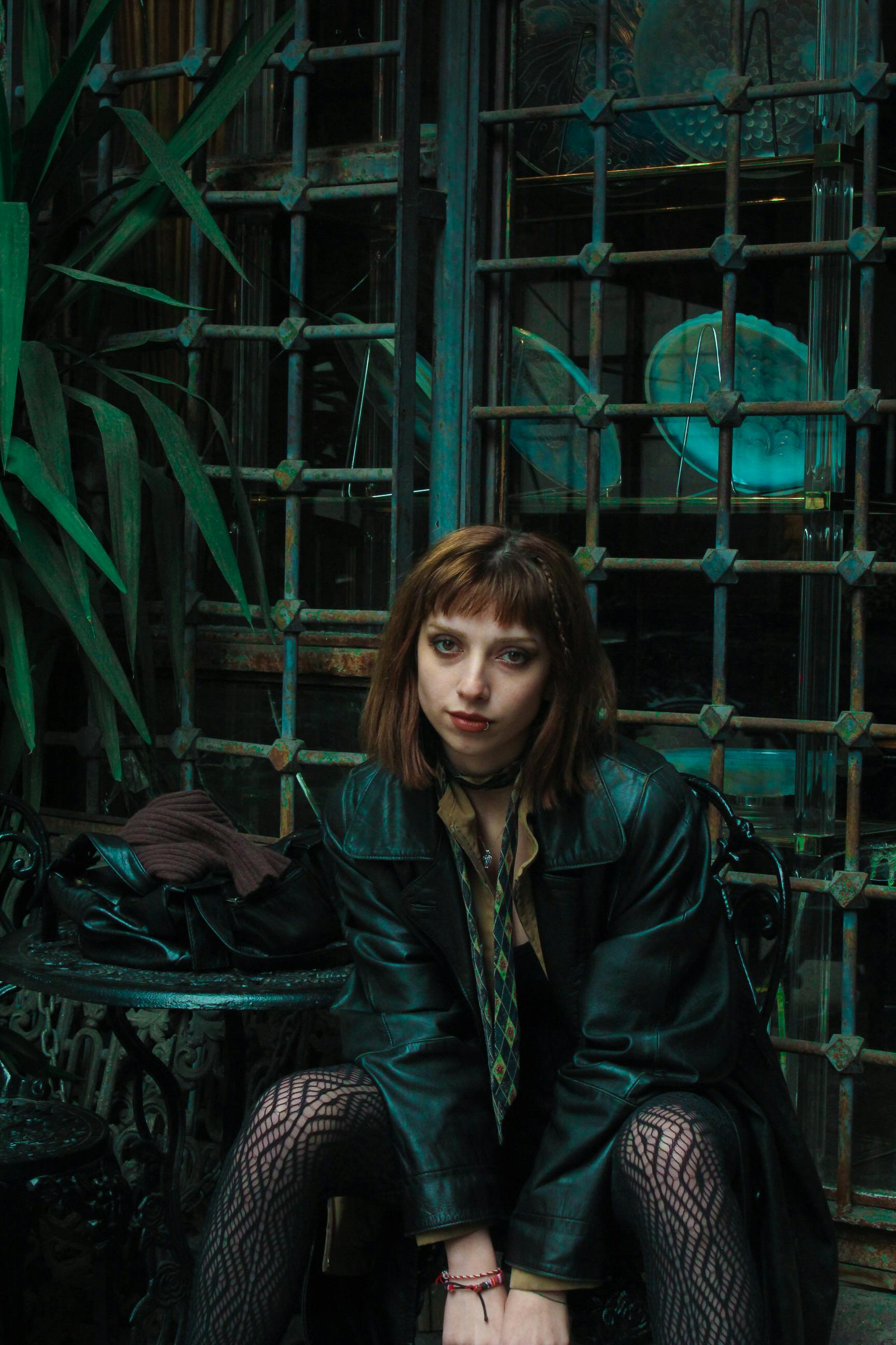 Portrait of a woman with dyed red hair sitting outdoors in a vintage setting.