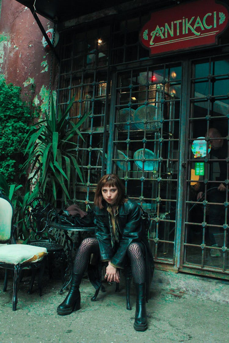 Green Toned Photo Of A Woman Sitting By A Vintage Shop With A Metal Bars