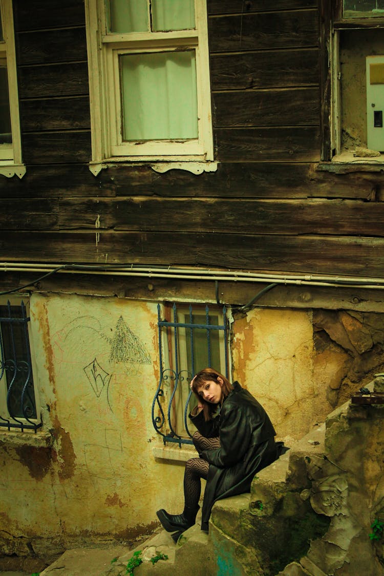 Yellow Toned Image Of A Woman Sitting On Steps By A Weathered House