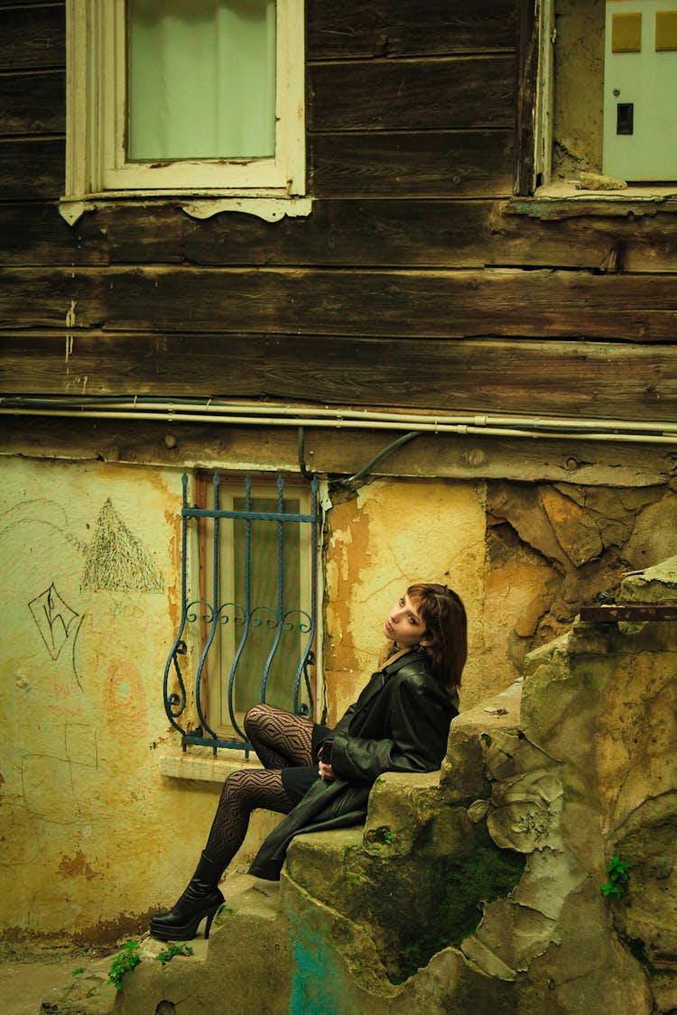 Yellow Toned Image Of A Woman Sitting On Steps By A Weathered House