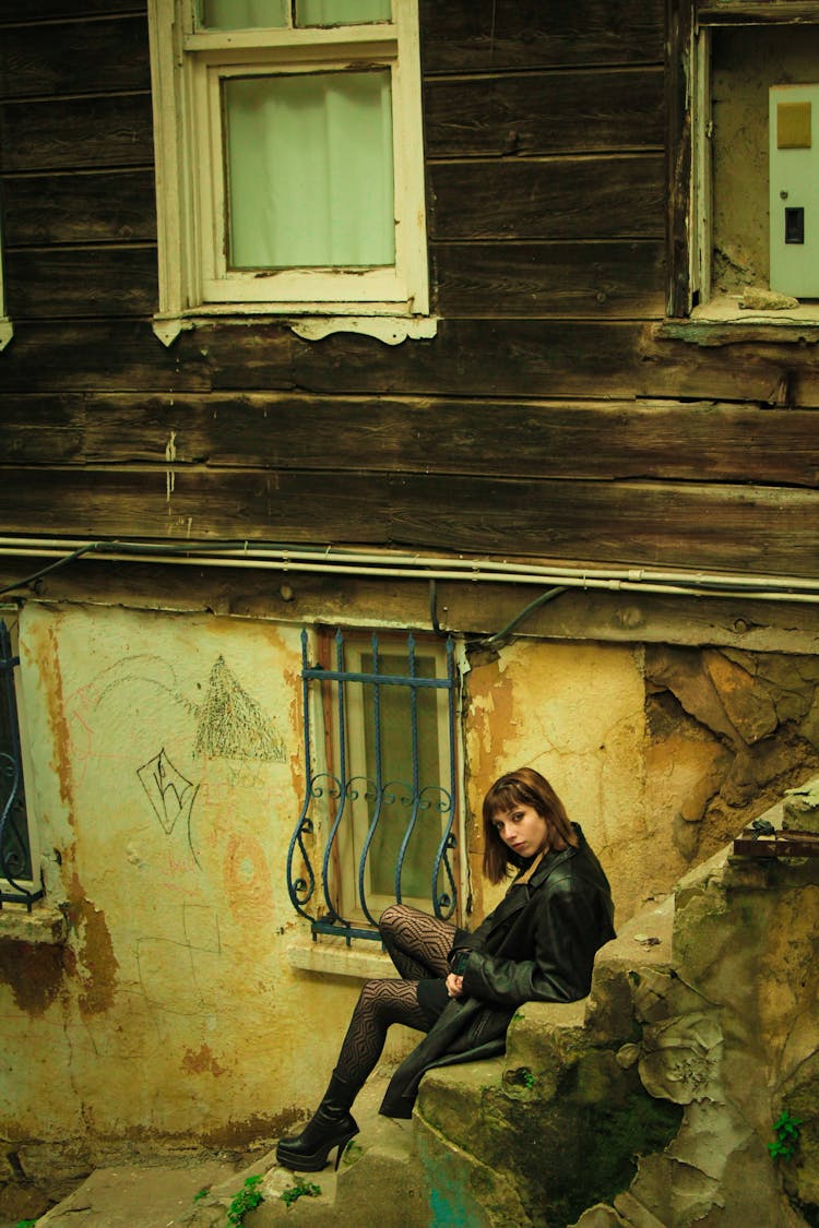 Yellow Toned Image Of A Woman Sitting On Steps By A Weathered House