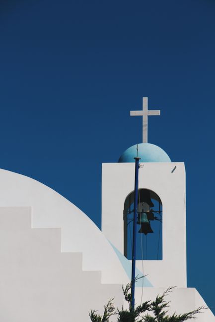 Minimalist photo of iconic white church with blue dome and cross in Santorini, Greece.
