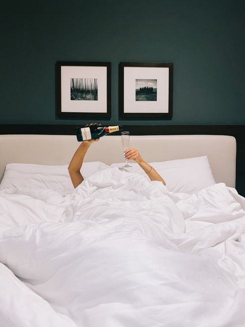 A person celebrates with champagne in bed, capturing a cozy and modern lifestyle vibe.