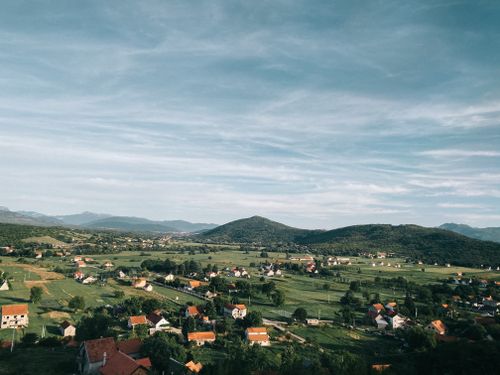 Free Aerial view of picturesque rural countryside with scattered houses and lush greenery under a clear sky. Stock Photo