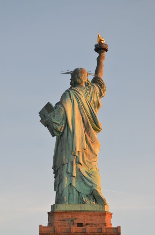 Free A striking view of the Statue of Liberty from behind, beautifully lit by the sunset in New York City. Stock Photo