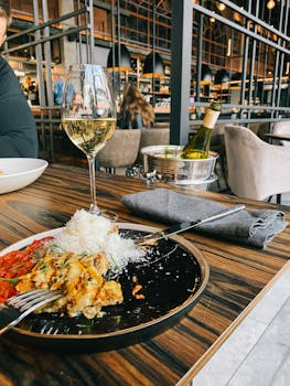 A tasteful dining setup in a modern restaurant, featuring a glass of white wine and a deliciously plated dish.