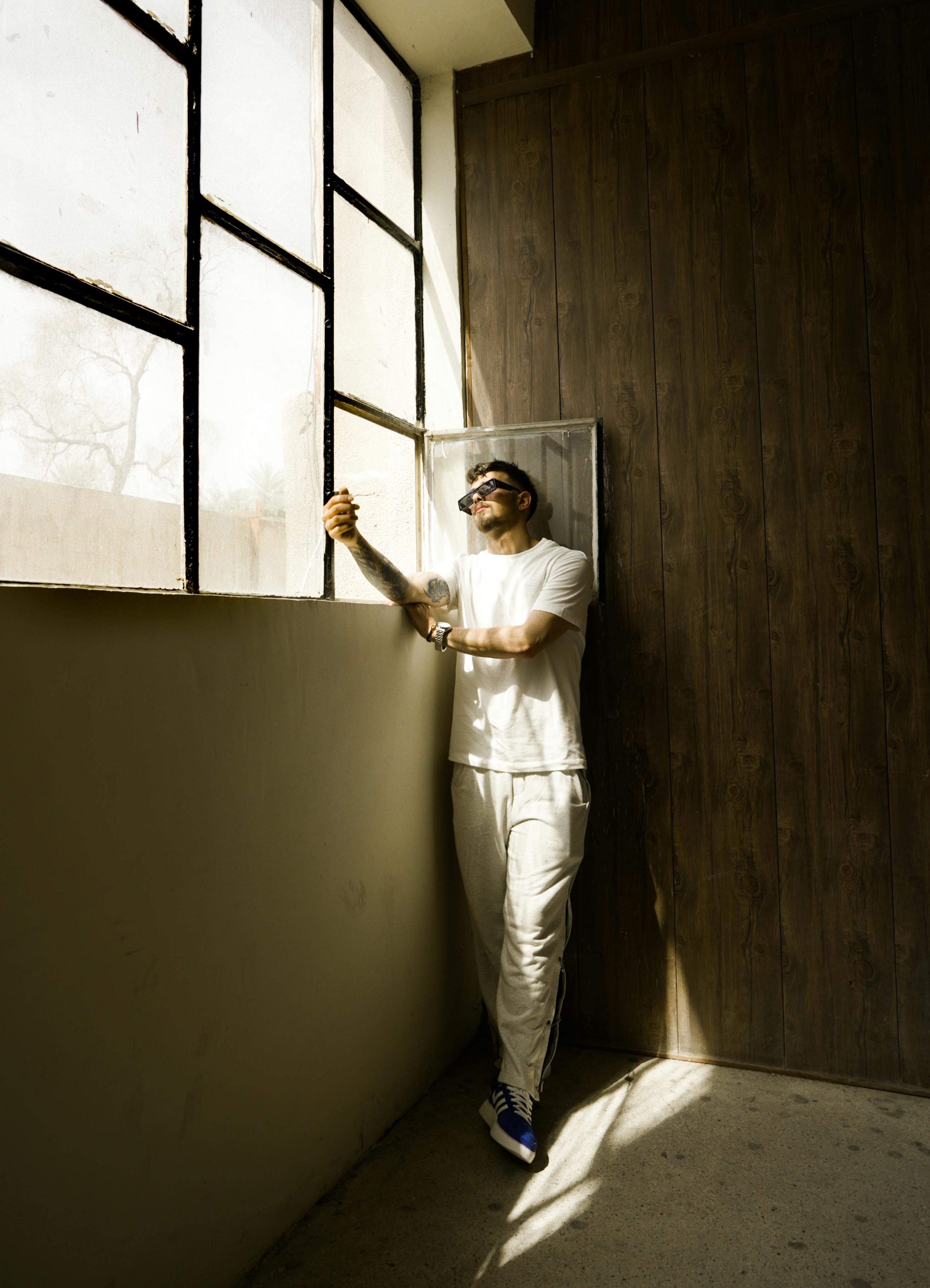 Free Caucasian man relaxing and leaning against window, bathed in sunlight. Stock Photo