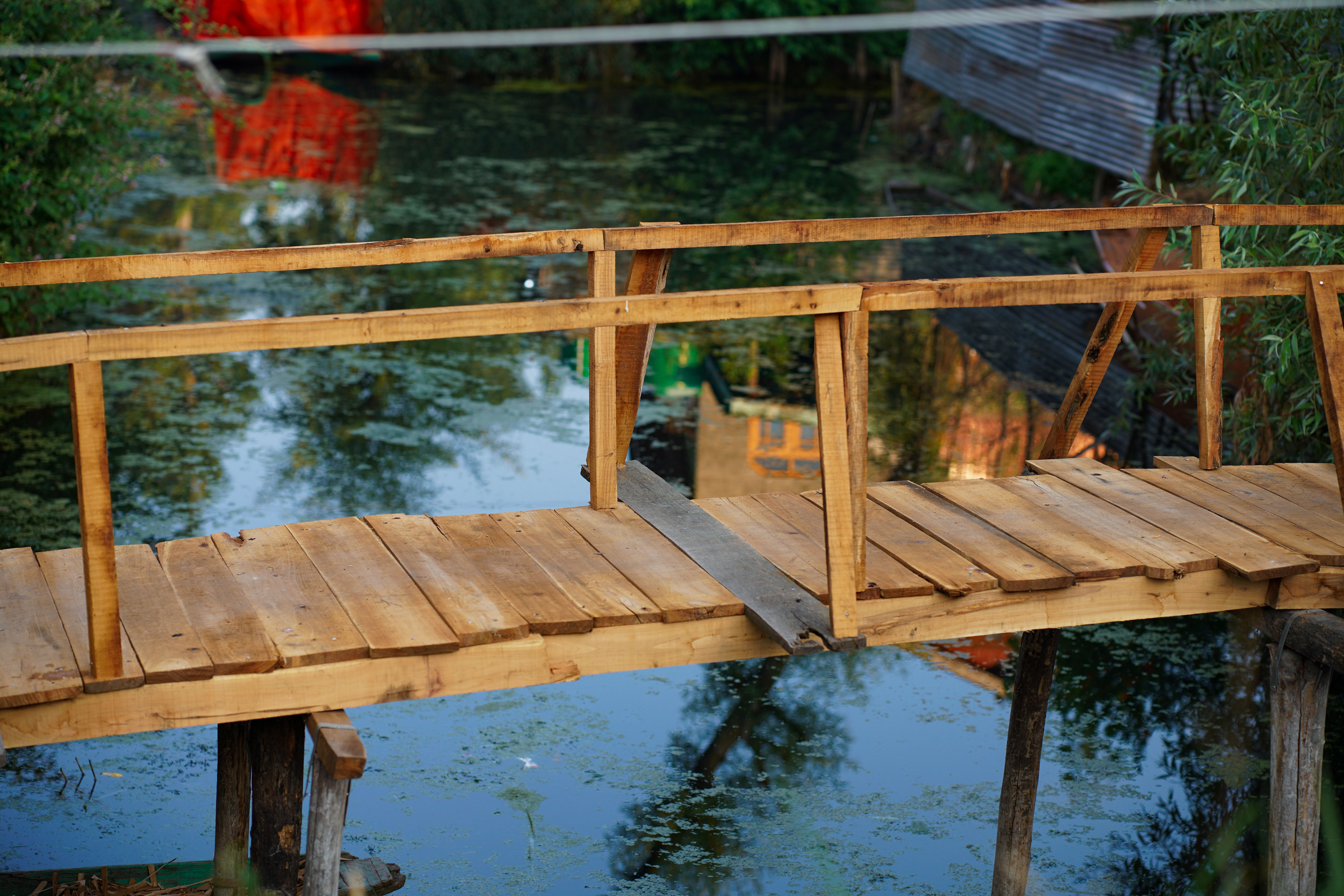 A rustic wooden footbridge spans a tranquil marsh landscape with reflections in the still water.