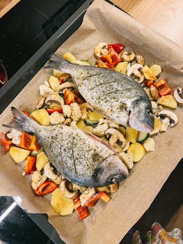 Fresh dorado fish with sliced vegetables ready to bake on parchment-lined tray.