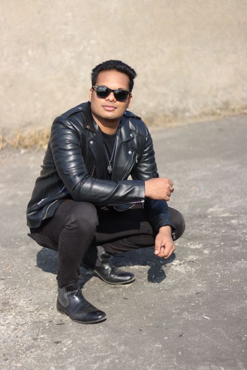 Free Fashionable young man wearing a leather jacket and sunglasses squatting on a sunny day outdoors. Stock Photo