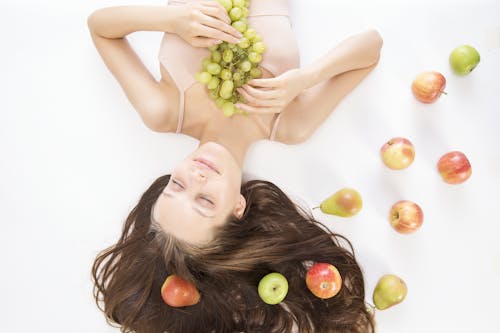 無料 床のクローズアップ写真でリンゴと梨の横にブドウの束を保持している女性 写真素材
