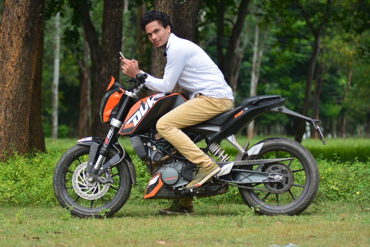 a man sits on a motorcycle in a lush forest park using a smartphone en