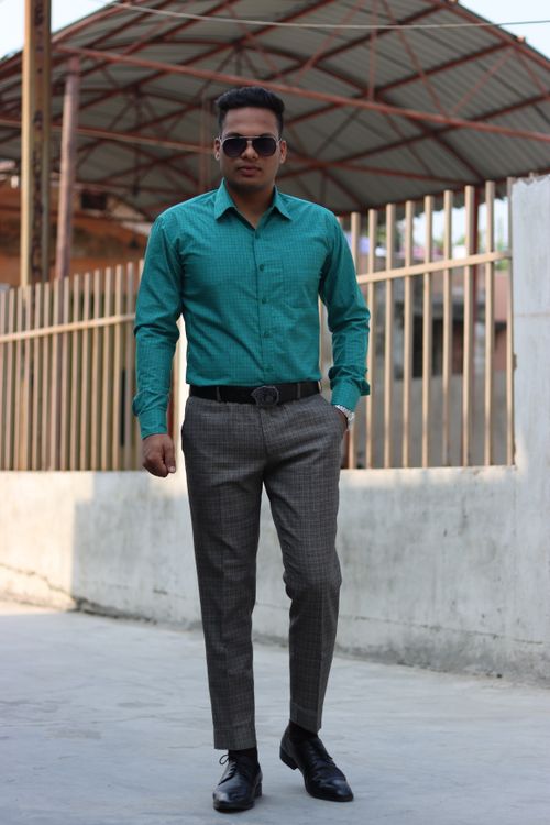 Free A fashionable man in a teal shirt and plaid pants stands confidently outdoors Stock Photo