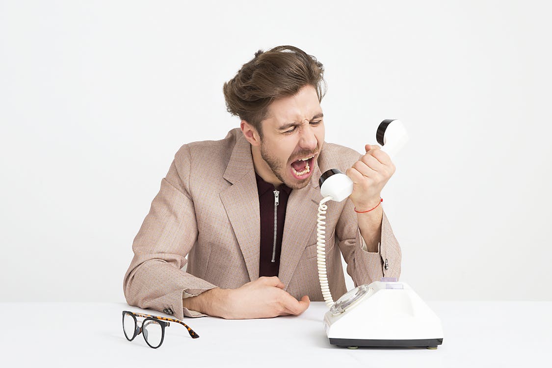 Man Wearing Brown Suit Jacket Mocking on White Telephone