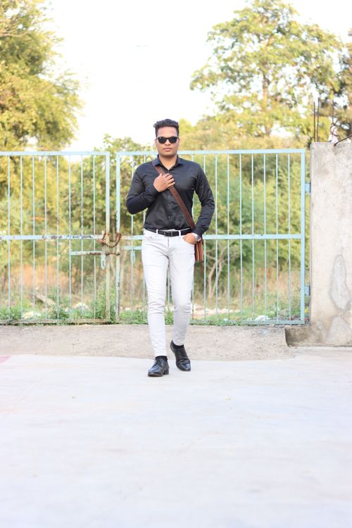 Free Confident man poses elegantly in front of a park gate against a natural backdrop. Stock Photo