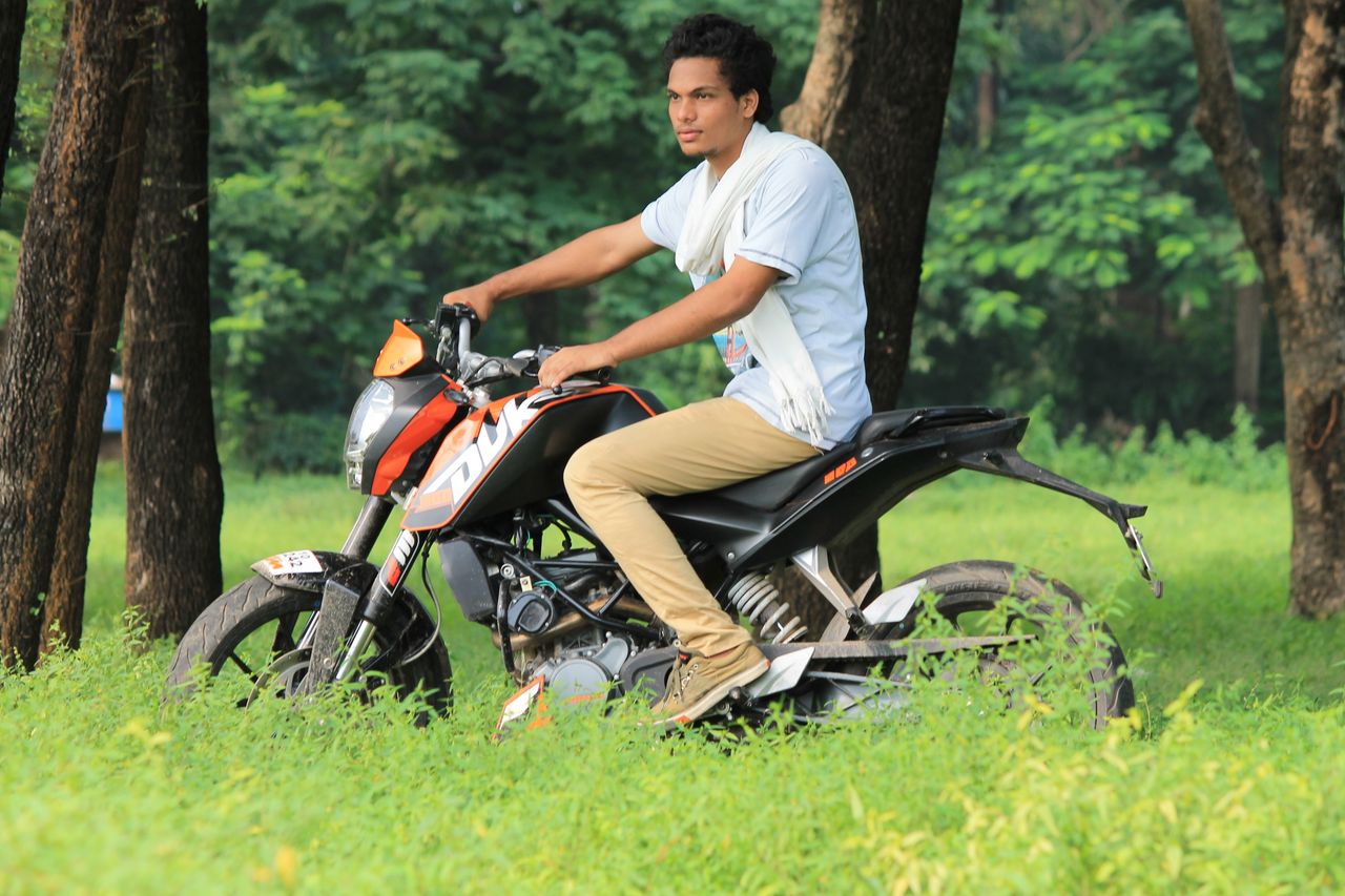 a young man leisurely riding a motorcycle through a lush green forest