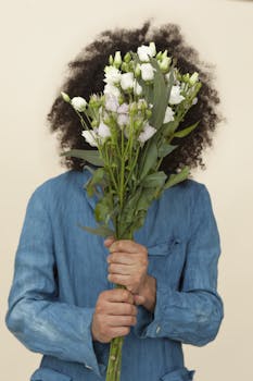 一个穿着蓝色衬衫的人拿着一束白花，遮住了脸