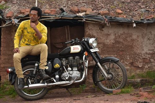 Free A man sits on a Royal Enfield motorcycle in a rustic, rural environment. Stock Photo