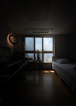 Modern bedroom interior with city view through large window, showcasing sunlight and shadows.