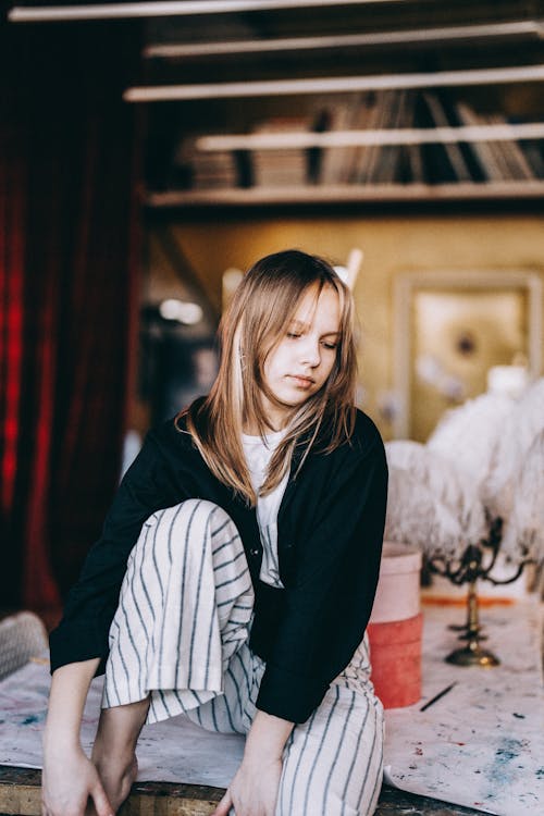 Blond Girl Wearing Striped Dungarees Sitting on a Table in a Studio