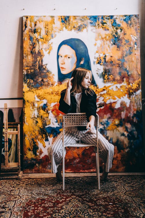 Woman Sitting Backward on Chair against Painting