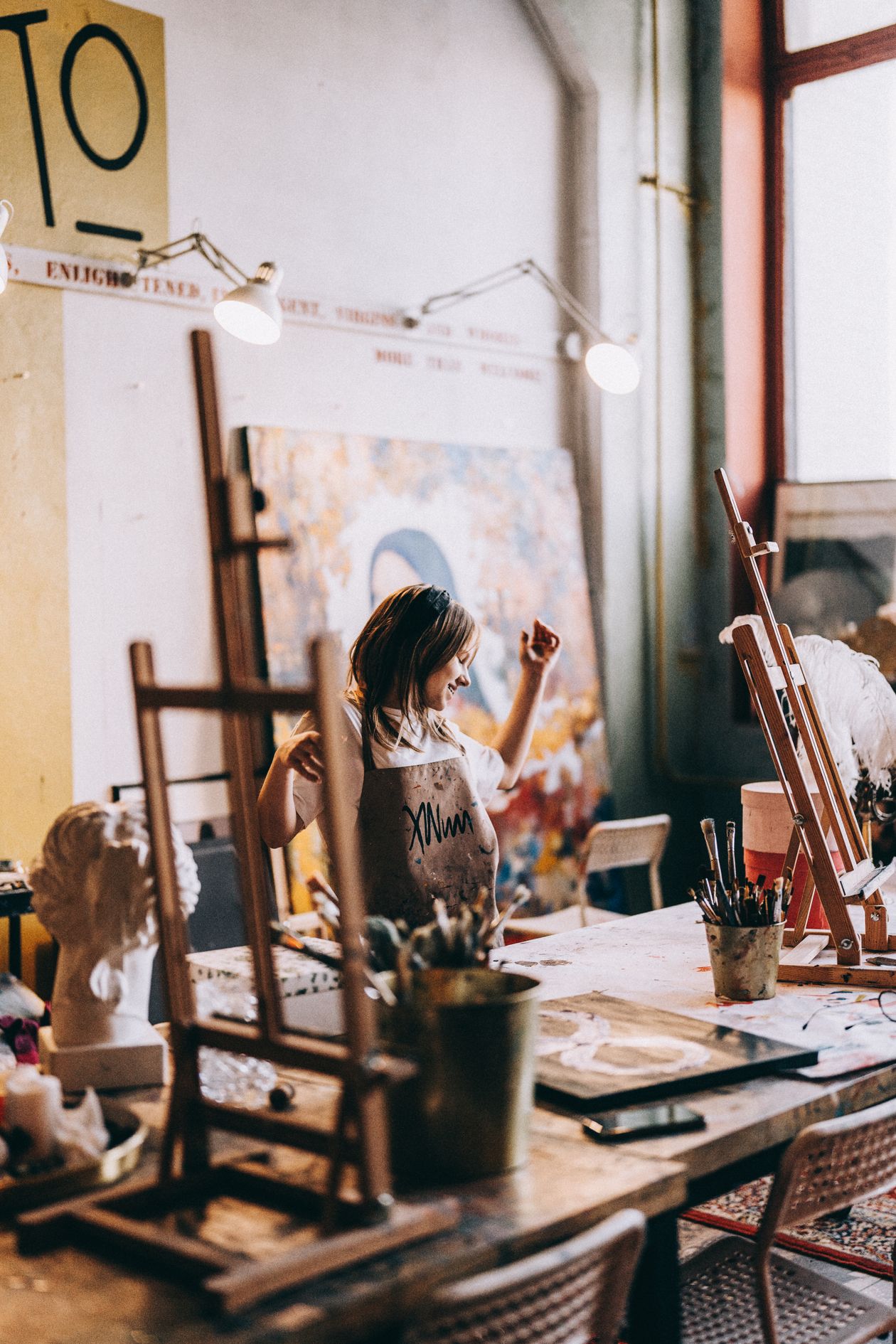 Sunlit restoration studio with easels, tall windows, and craftspeople at work