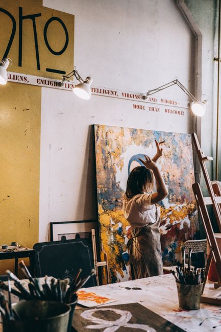 A woman artist engrossed in painting a large abstract canvas in her art studio, surrounded by tools.