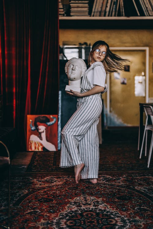 Woman in Striped Dungarees Dancing with Sculpture