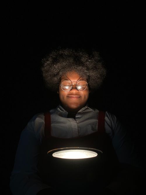 Free A cheerful person with eyeglasses and curly hair smiles while holding a flashlight in the dark. Stock Photo