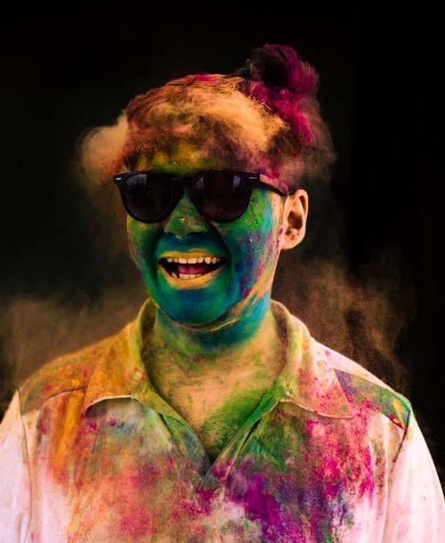 Free An adult celebrating Holi with vibrant colors and a joyful smile, wearing sunglasses. Stock Photo
