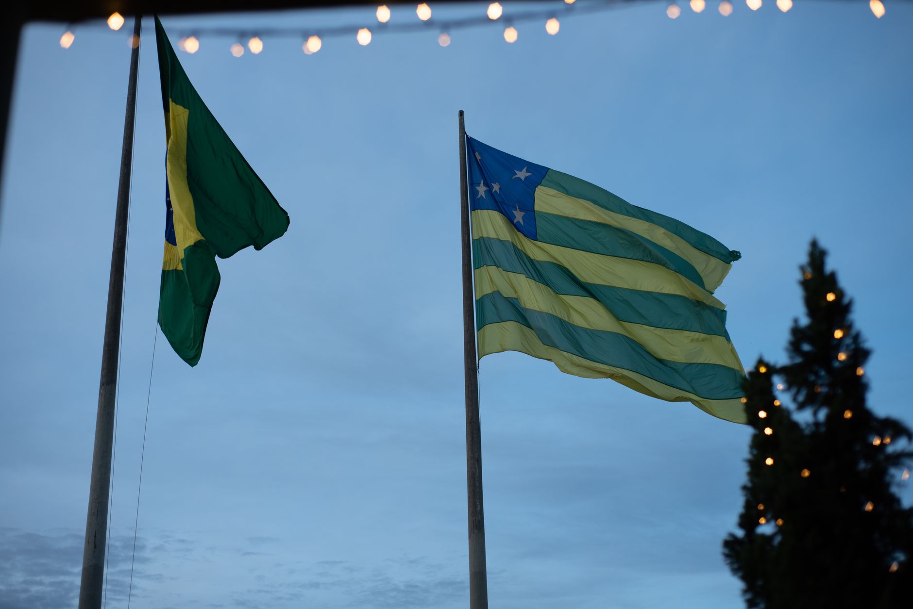 Brazil and Goiás flags waving against a twilight sky adorned with festive lights.
