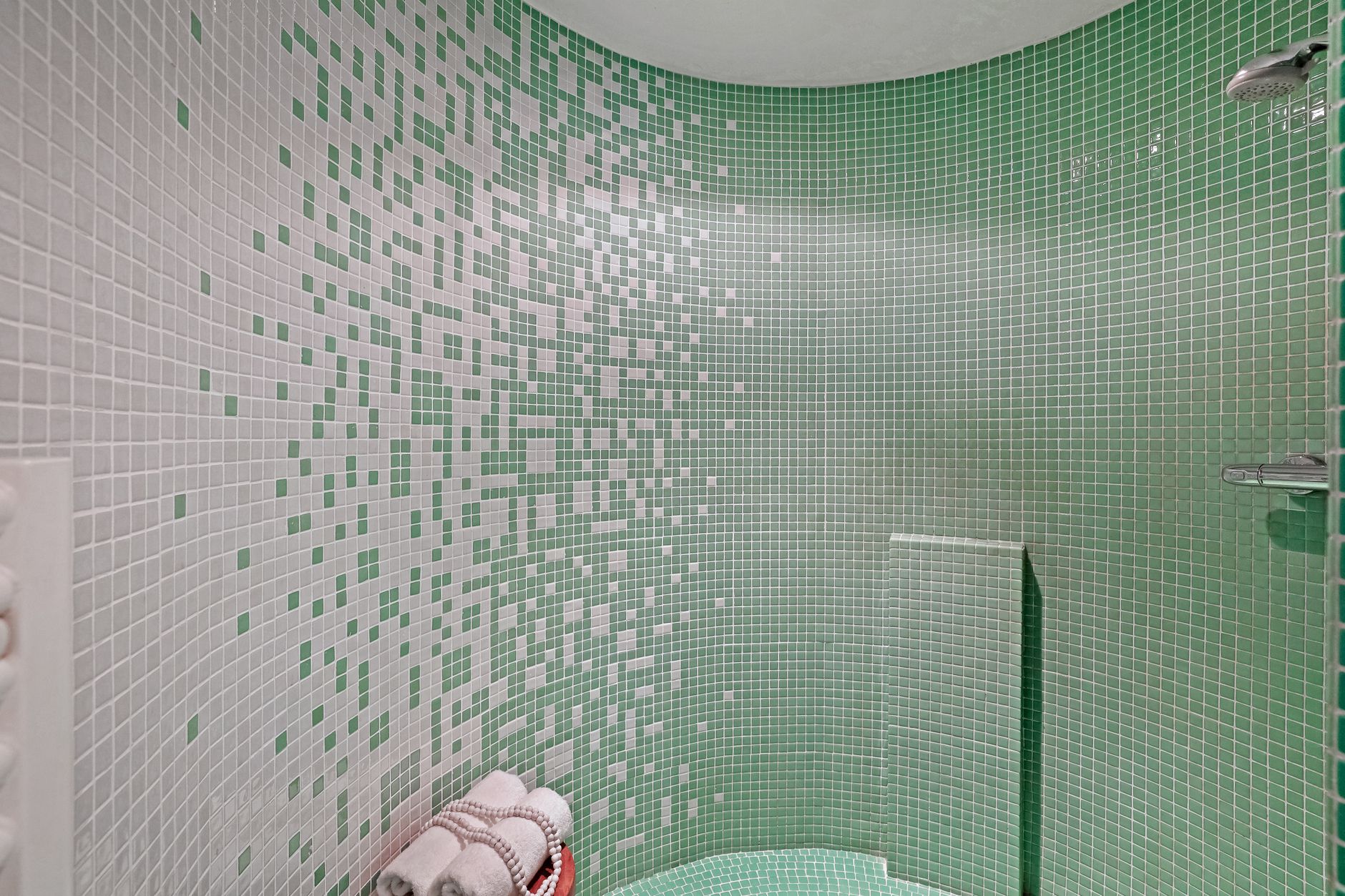 A stylish small bathroom with green and white mosaic tiles and a neatly folded towel set.