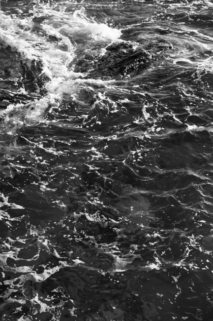 Captivating black and white image of ocean waves crashing against rocks, creating a dynamic seascape.