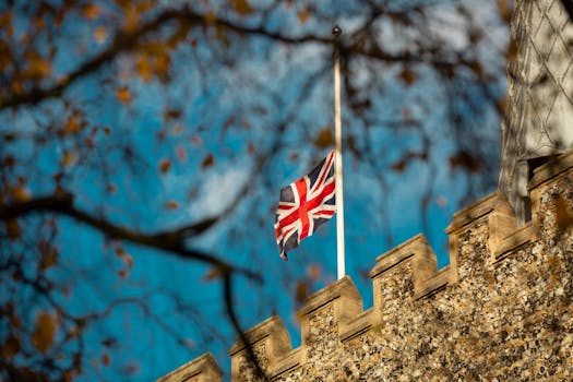 Union Jack flag fluttering atop a historic stone castle on a sunny autumn day.