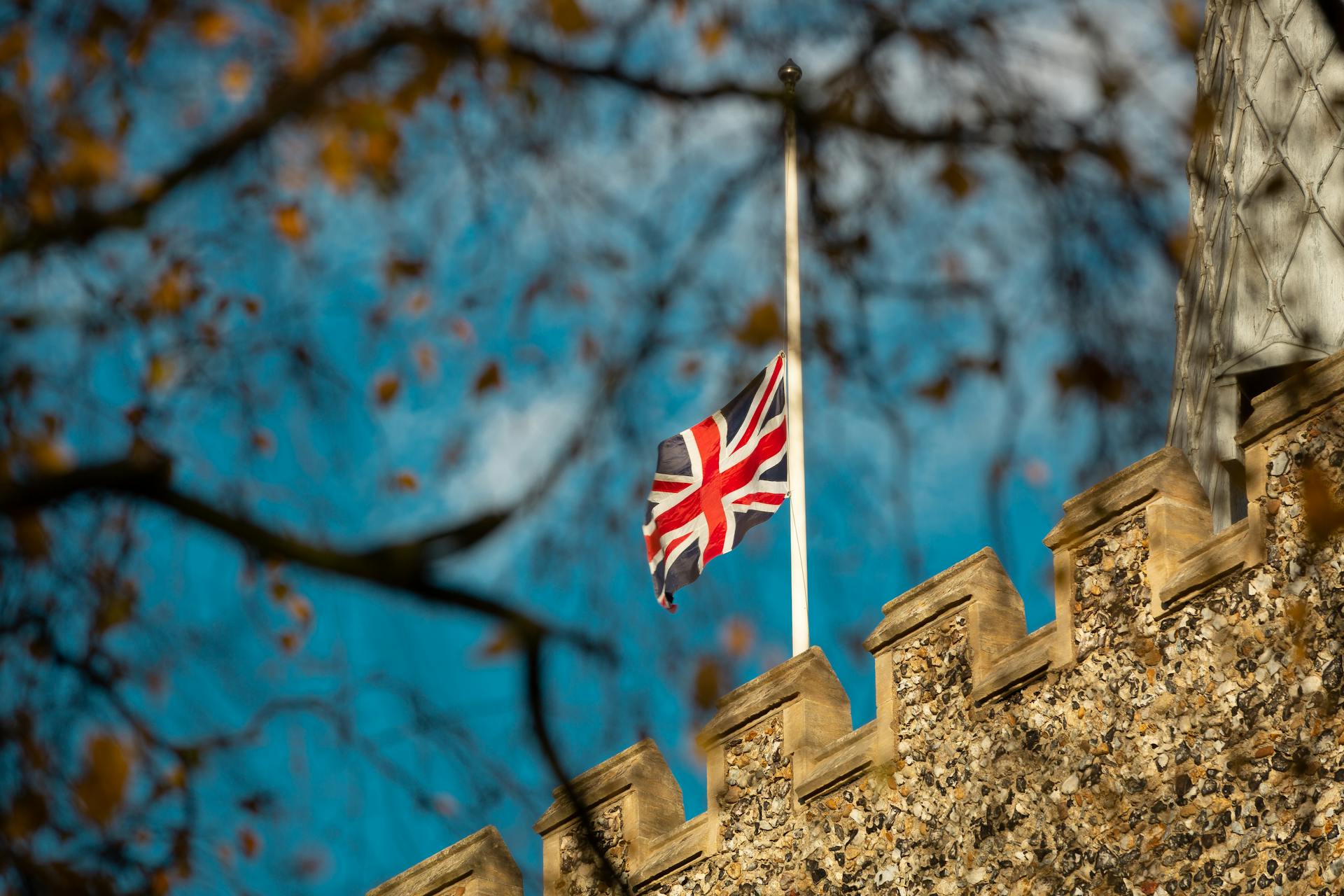 Union Jack flag fluttering atop a historic stone castle on a sunny autumn day.