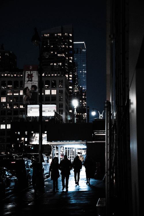 Free High contrast cityscape with silhouettes of people walking at night under bright city lights. Stock Photo