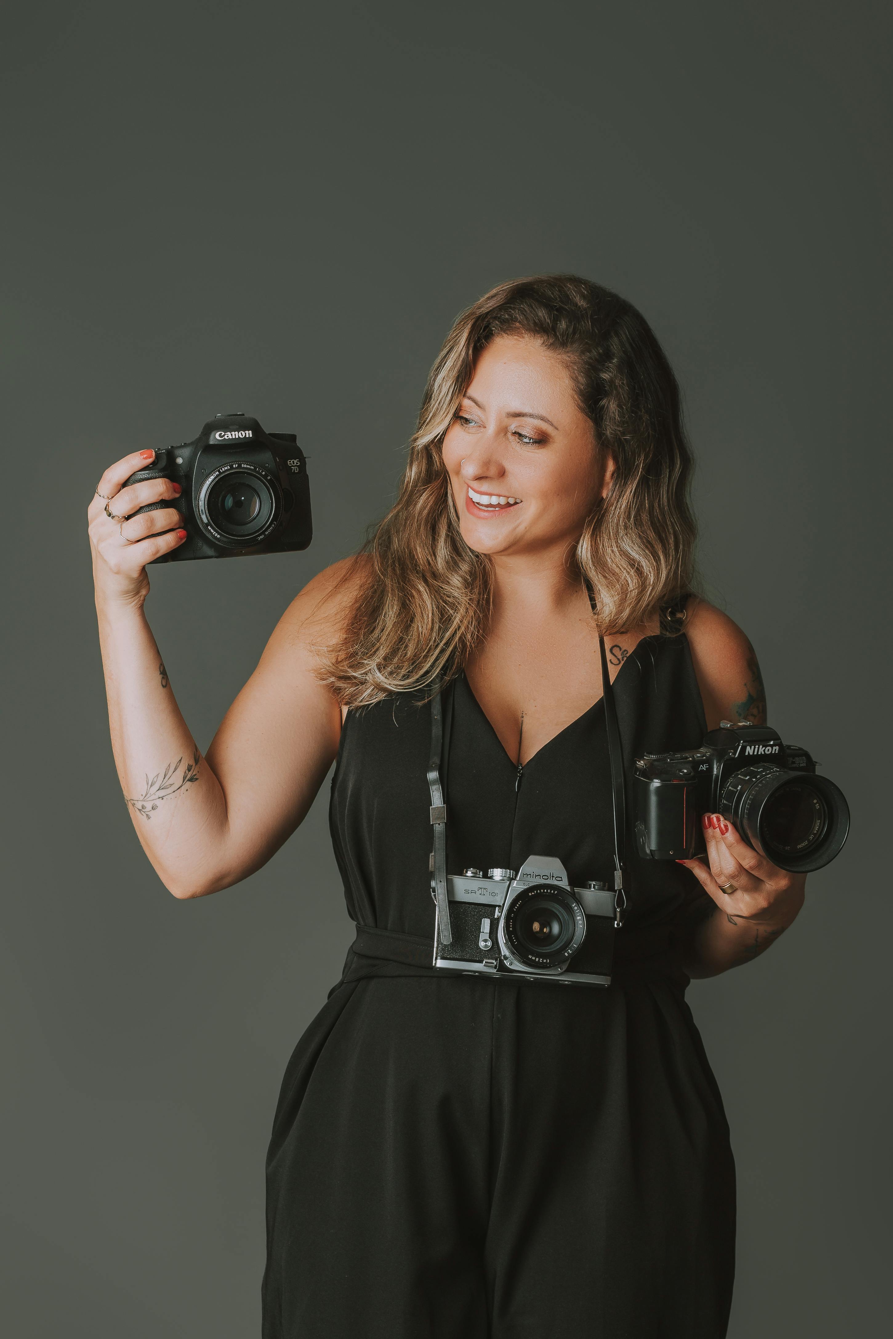 Portrait of a smiling woman holding cameras, showcasing photography passion.