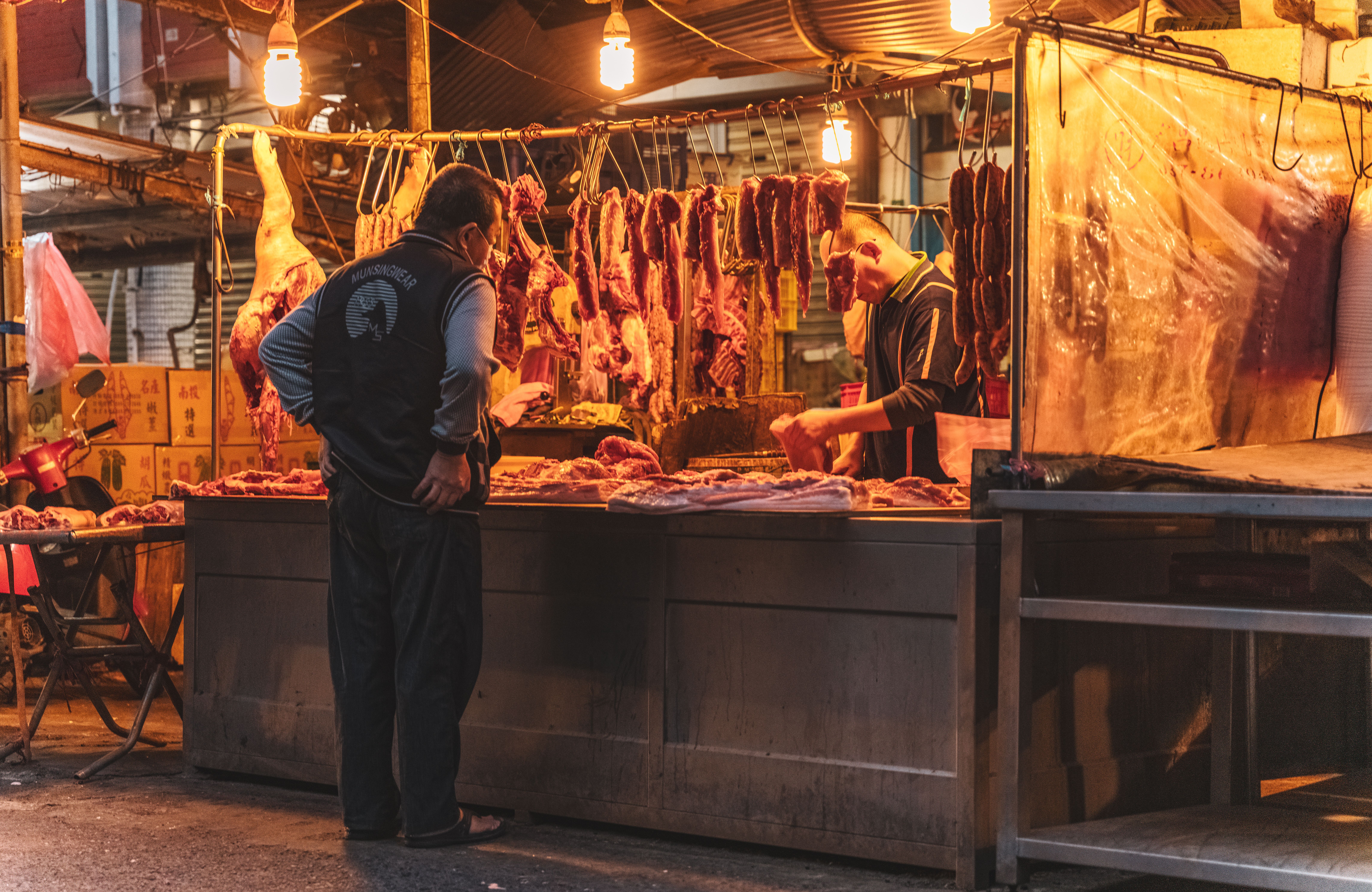 A vendor and customer at a meat market stall in Taiwan during dusk.