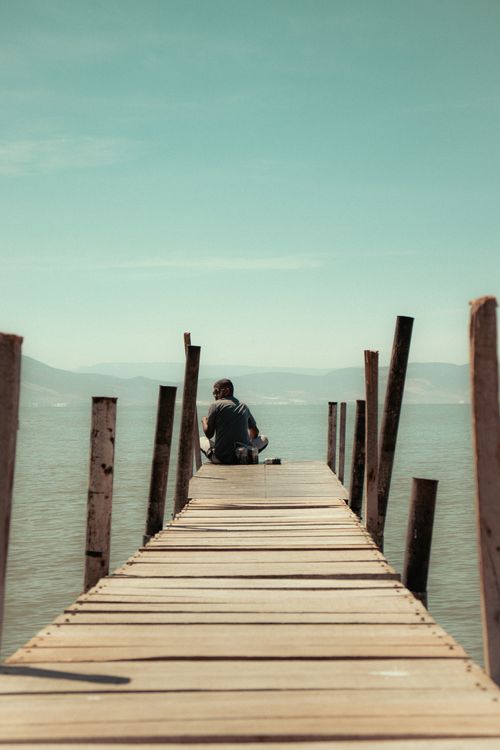 Free A man sits on a wooden pier overlooking Lake Chapala under a clear blue sky. Stock Photo