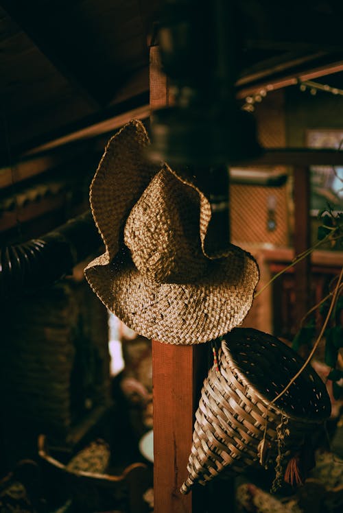 A Hat and Woven Basket Hanging on a Wooden Pole 