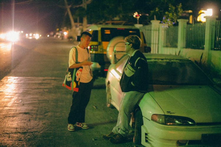 Young Men Standing Next To A Car At Night And Talking 