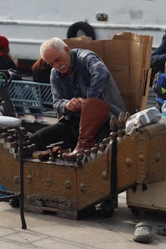 Elderly shoeshiner polishing a boot in an urban setting, focusing on craftsmanship and tradition.