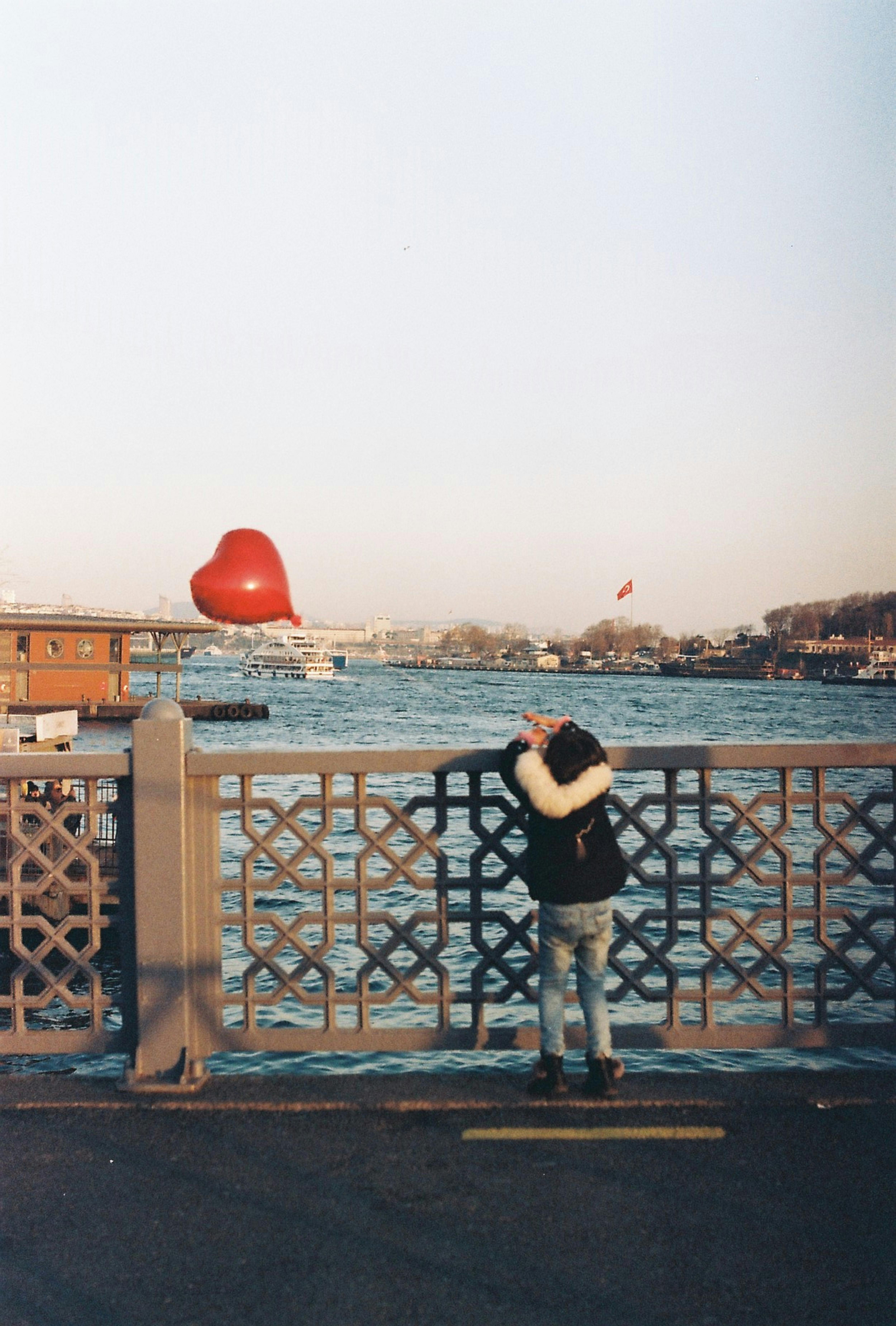 A child gazes over the Bosporus holding a heart-shaped balloon on a bridge in Istanbul, Turkey.