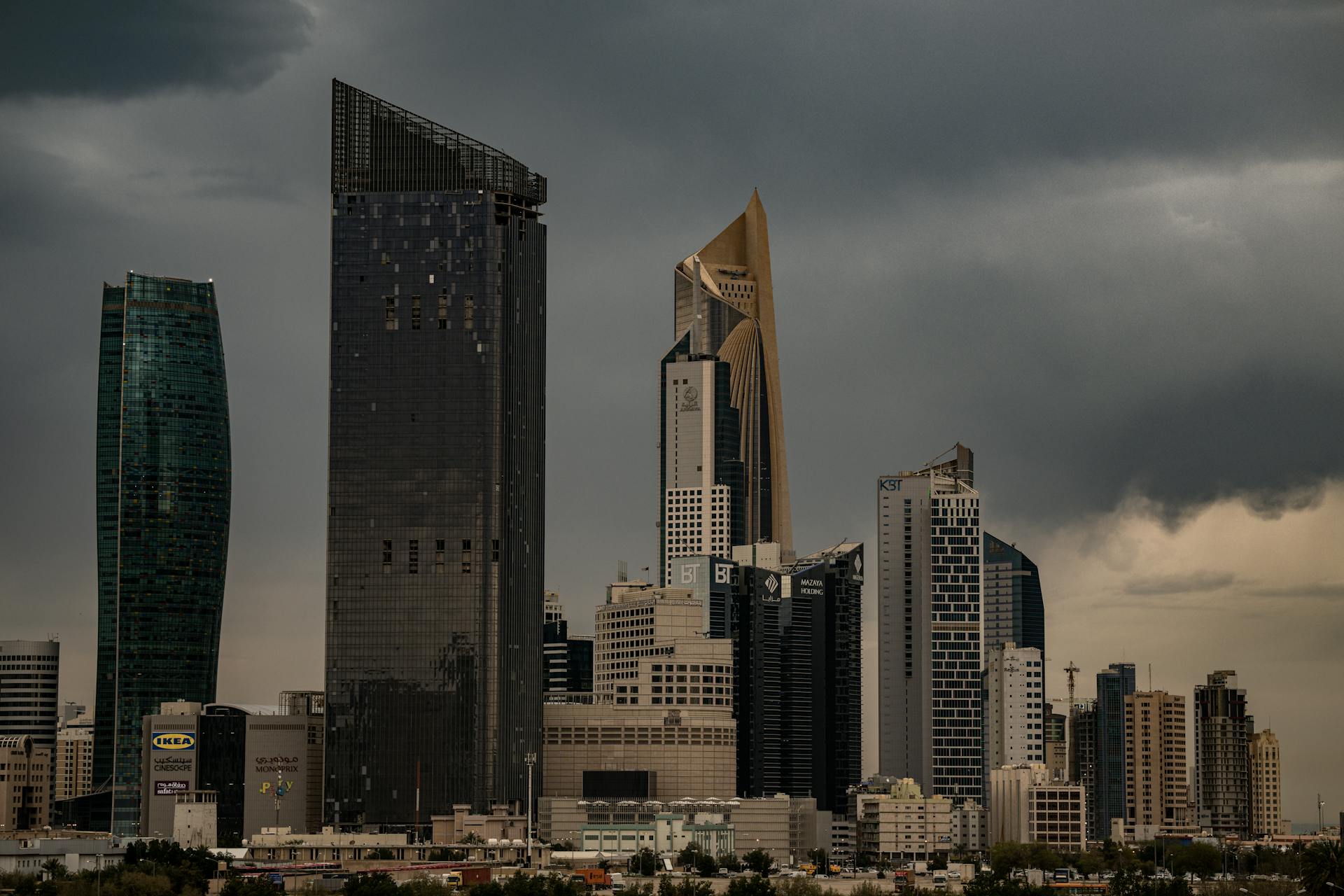 A moody Kuwait City skyline with towering skyscrapers under a cloudy sky.